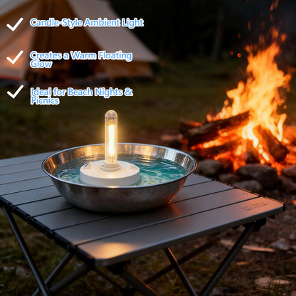 Floating water-powered lantern glowing in a metal bowl on a camping table with a bonfire and tent in the background.